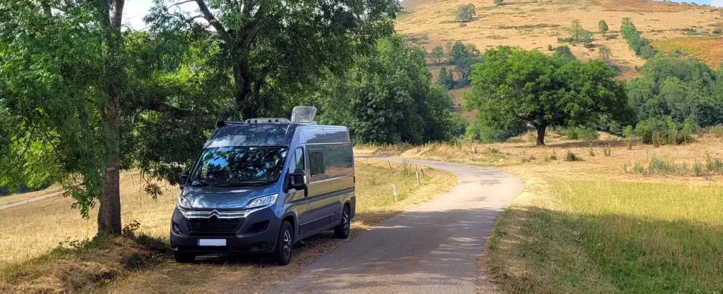Fourgon aménagé bleu stationné sous arbre en bord de route